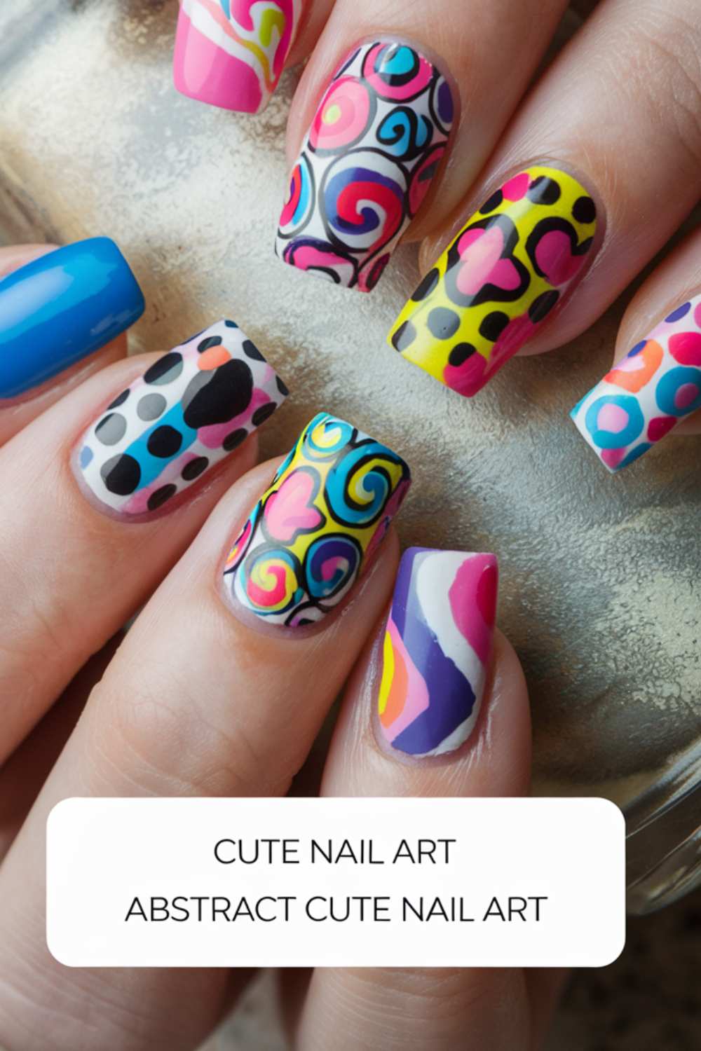 A close-up of a hand showcases nails adorned with vibrant, abstract patterns. Swirls, hearts, and geometric shapes dance across each nail in lively hues of pink, blue, yellow, and black. The text below declares Abstract Cute Nail Art for those who embrace unique charm.