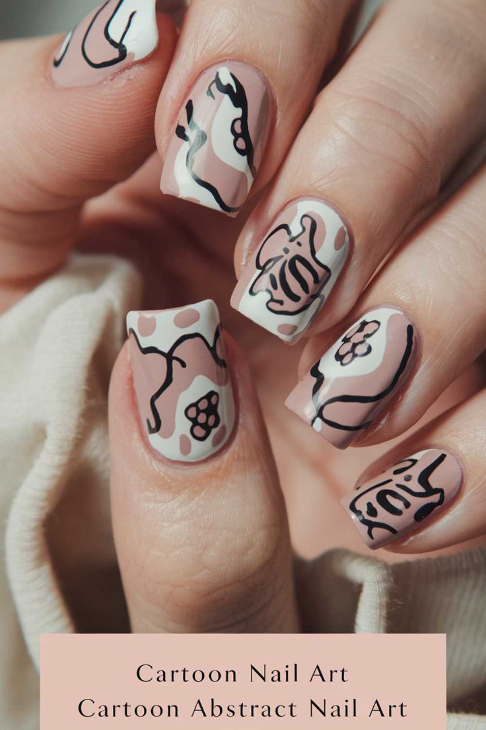Fingers flaunt square-shaped nails adorned with cartoon nail art designs in black on a soft pink base. The playful, abstract line art patterns add a charming touch to each nail, creating a delightful visual treat.
