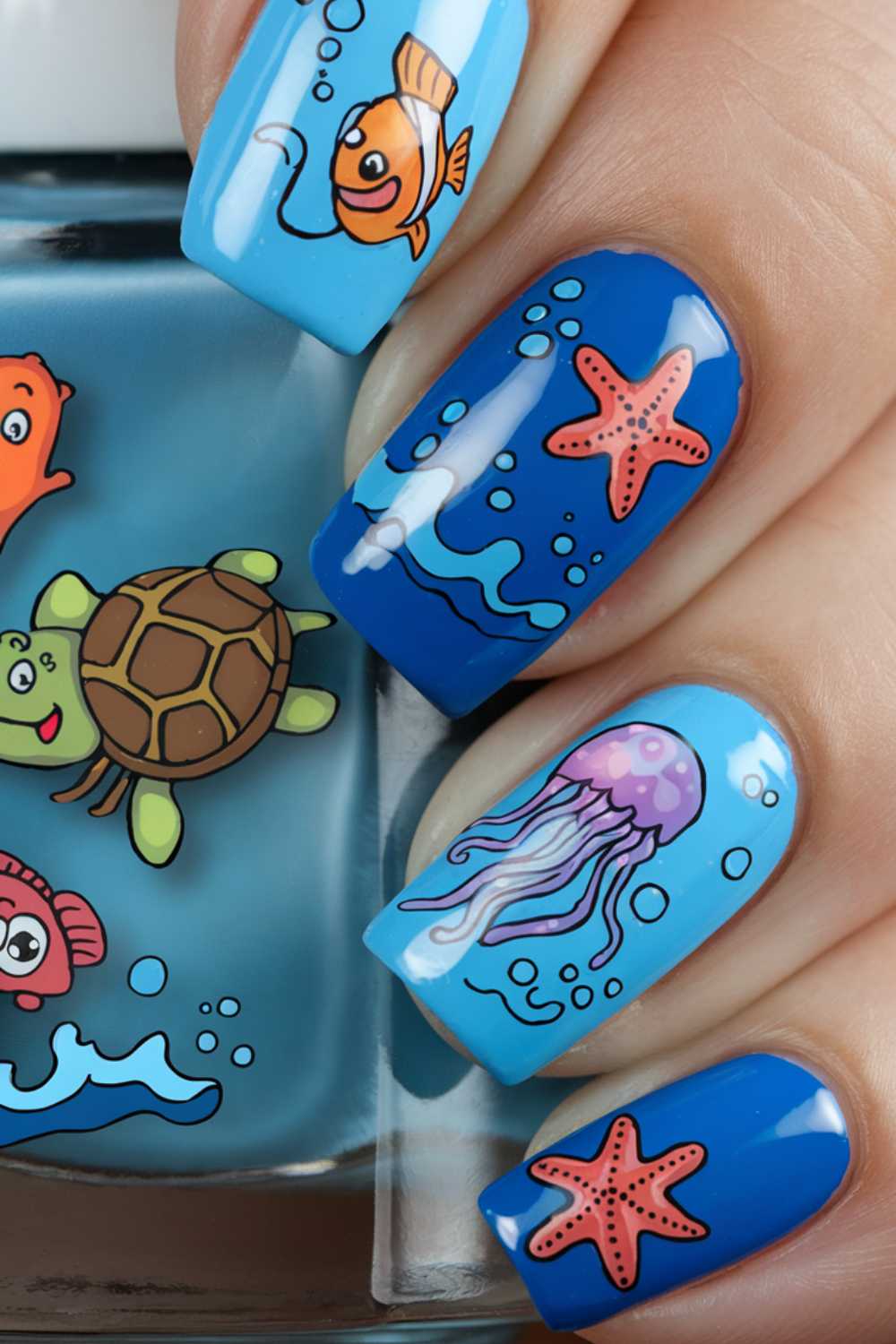 Close-up of a hand showcasing vibrant cartoon nail art designs. The aquatic-themed nails feature playful depictions of a clownfish, turtle, jellyfish, starfish, and sea waves, all in bright colors against a blue background.