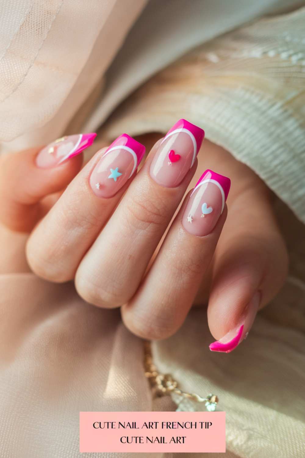 A hand displays vibrant pink French tip nails adorned with cute heart and star designs on a pale pink base, set against a soft beige fabric backdrop.