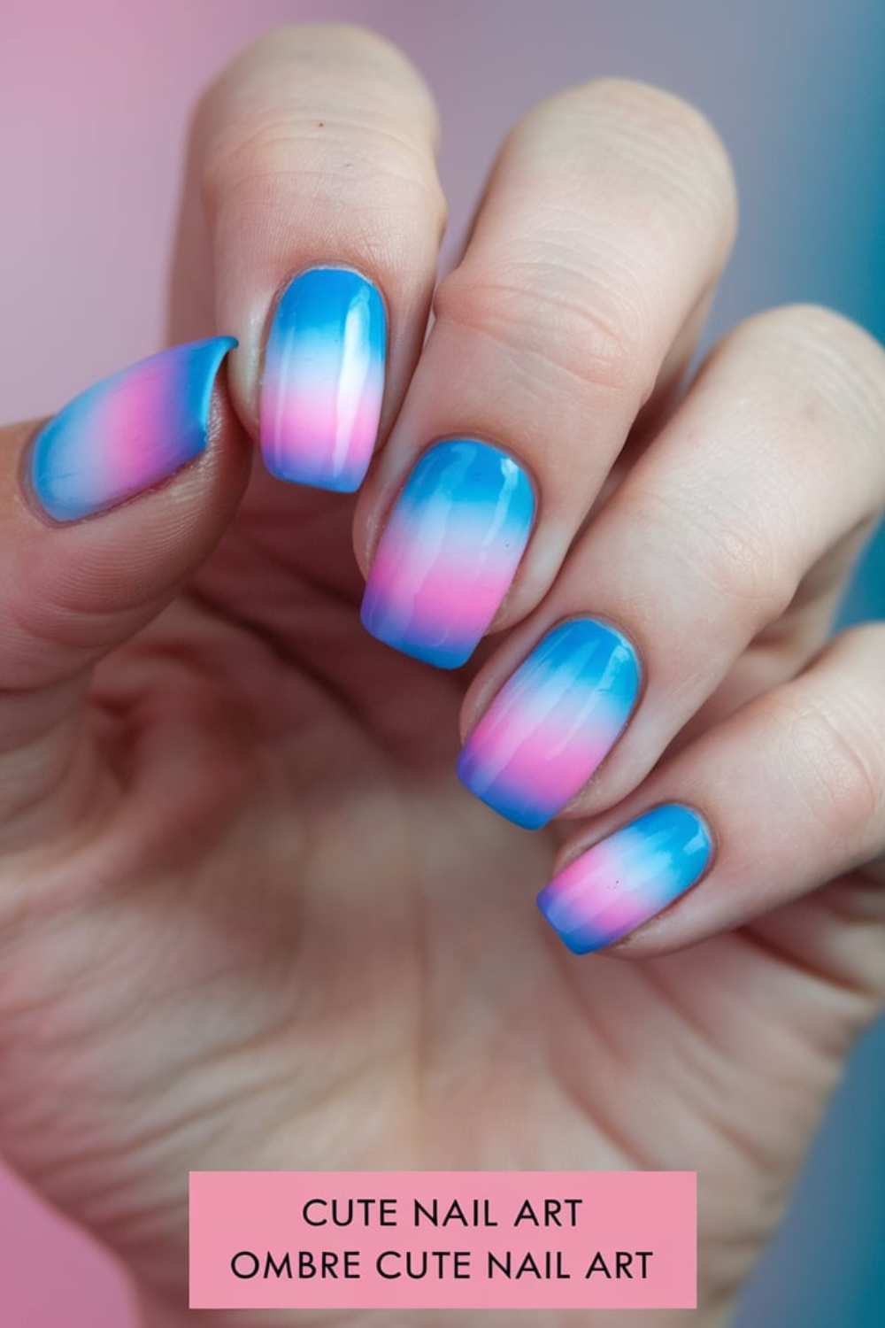 A close-up of a hand showcases nails with a delightful blue and pink ombre design, epitomizing cute nail art. The smooth, glossy finish transitions seamlessly from blue to pink, with a text overlay at the bottom reading Cute Nail Art Ombre Cute Nail Art.