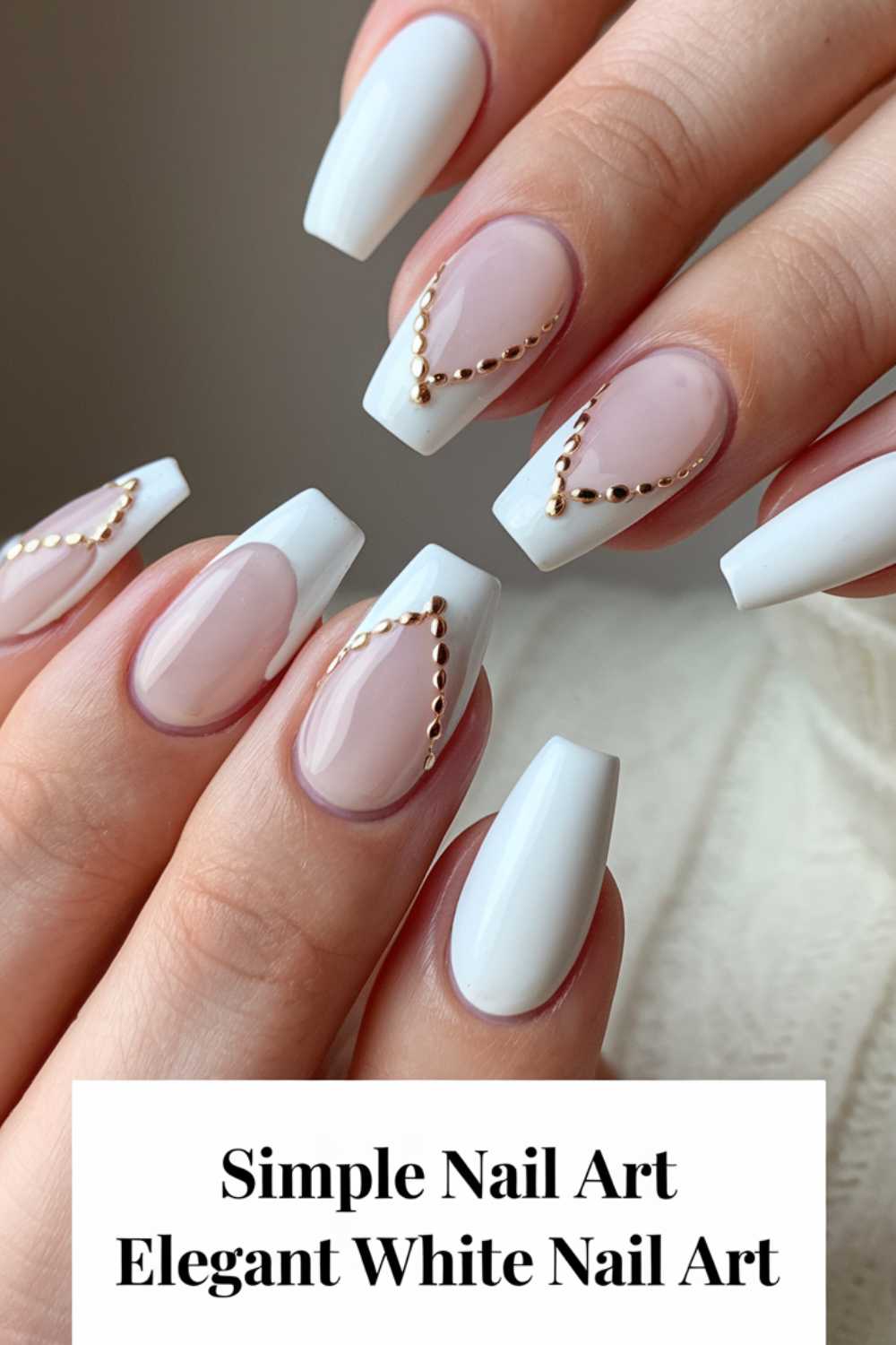 Hands with long white nails featuring clear sections and gold bead accents display simple nail art at its finest. The thumb and middle fingers boast elegant V-shaped designs, making this white nail art truly standout.
