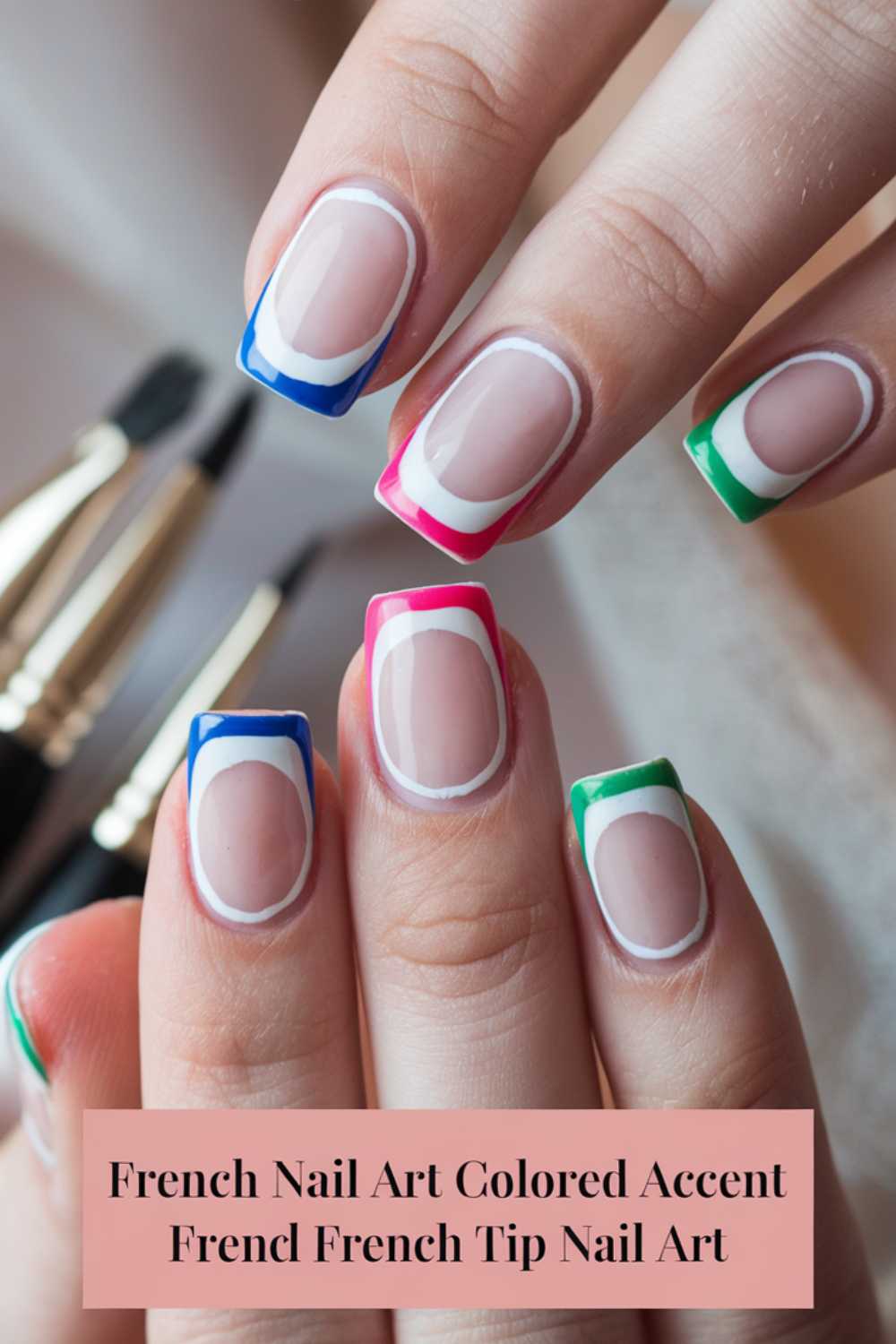 Close-up of hands with a stylish French manicure featuring colored accents in blue, pink, and green on almond-shaped nails. Three nail brushes are blurred in the background. Text at the bottom reads: French Nail Art Colored Accent French French Tip Nail Art.