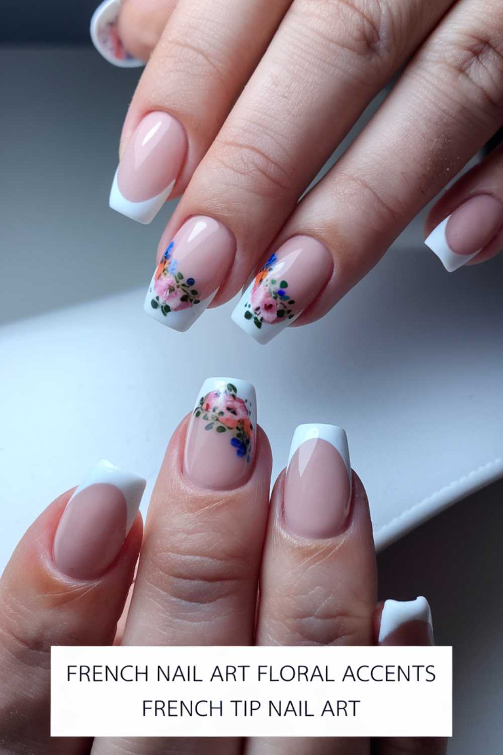 Close-up of hands showcasing French tip nails. Each nail has a white tip with a floral design featuring pink and blue flowers on an accent nail. Text reads: FRENCH NAIL ART FLORAL ACCENTS FRENCH TIP NAIL ART.