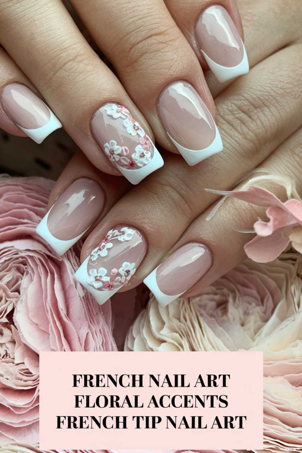 Hands with French tip nails resting on soft pink flowers. The nails are square-shaped with white floral accents on a few. The caption below reads French Nail Art, Floral Accents, French Tip Nail Art.