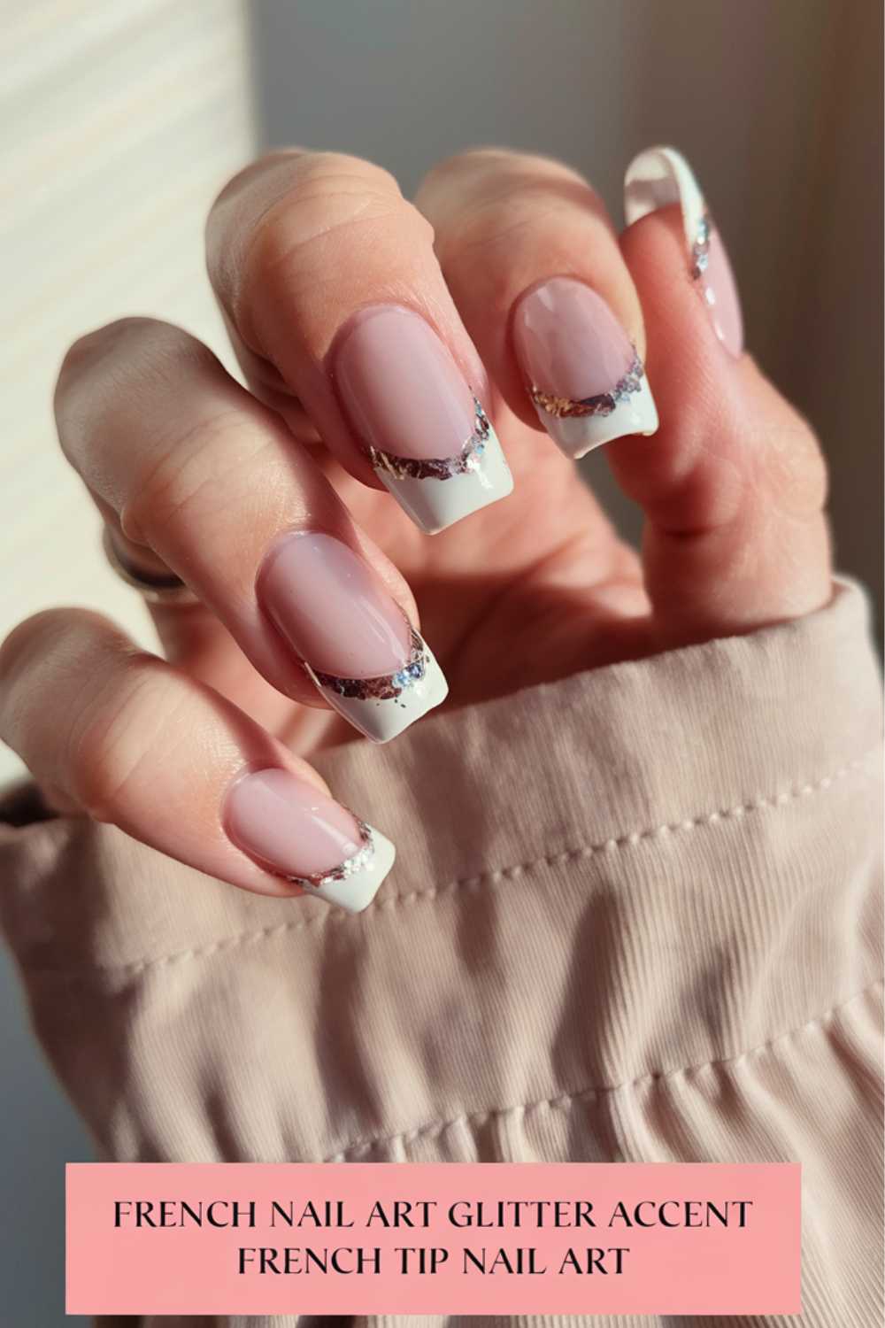 A hand with nude-pink French tip nails featuring a glitter accent. The nails have a shiny finish, and the hand is partially covered by a beige sleeve. Text at the bottom reads, French Nail Art Glitter Accent, French Tip Nail Art.