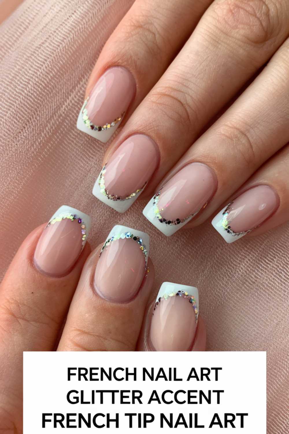 Close-up of manicured hands with French tip nail art. Nails have white tips and are accented with a subtle glitter line. The background is a light pink fabric. Text at the bottom reads: FRENCH NAIL ART GLITTER ACCENT FRENCH TIP NAIL ART.