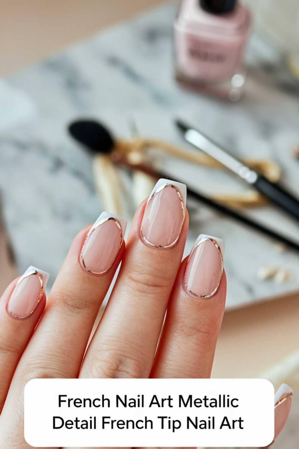 Close-up of a hand with a chic French manicure featuring metallic details along the white tips. In the background, nail polish, a brush, and grooming tools are visible on a marble surface.