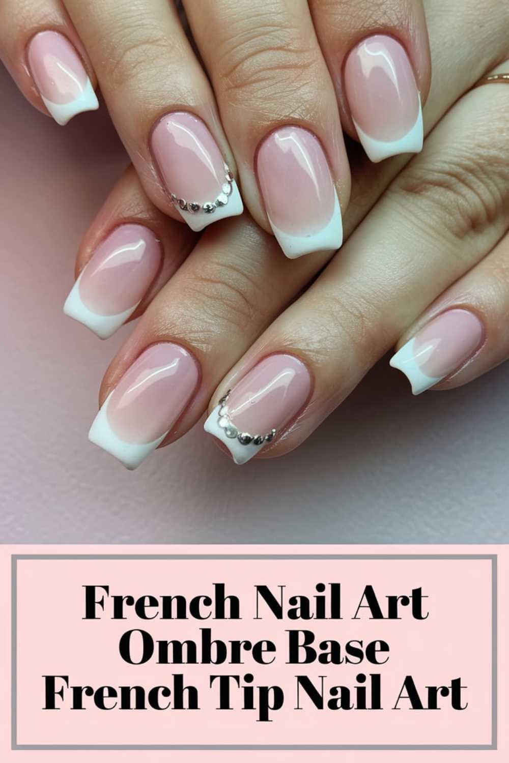Close-up of hands with French manicure. The nails have an ombre pink base and white tips, featuring small silver embellishments on accent nails. Below, text reads French Nail Art Ombre Base French Tip Nail Art.
