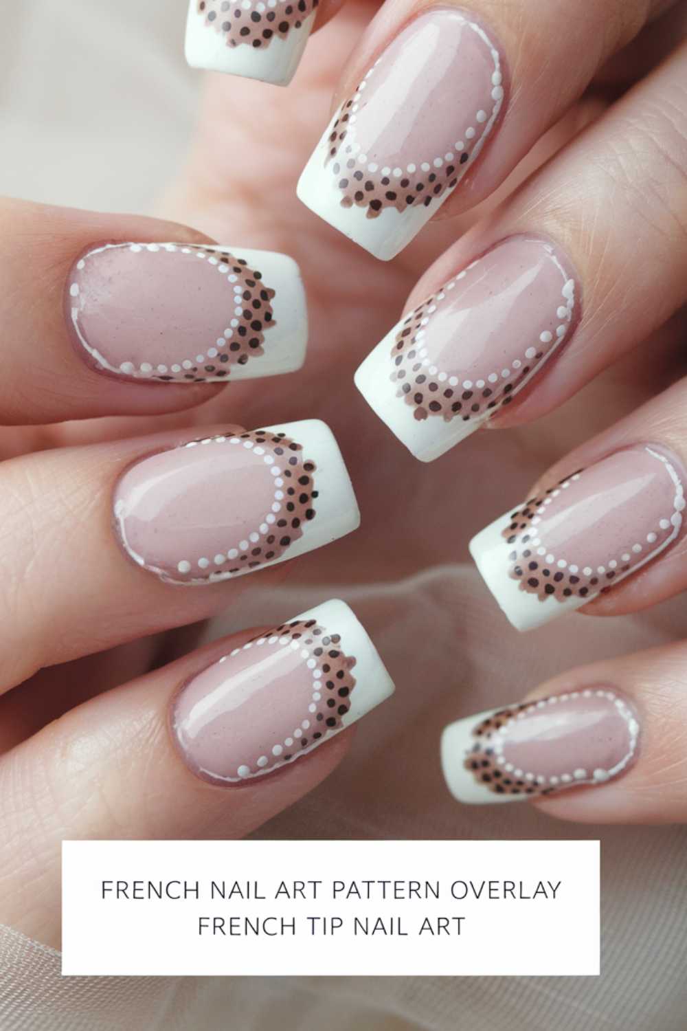 Close-up of a hand featuring French tip nails with intricate brown and white dotted patterns on a light pink base. The nails are glossy and neatly manicured.