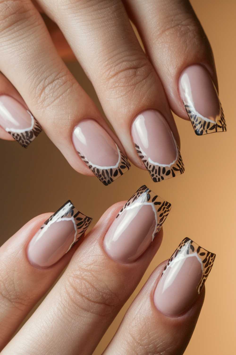 Close-up of hands featuring a manicure with nude polish and intricate leopard print tips. The design combines glossy nude and detailed black animal patterns at the tips for a sophisticated look.