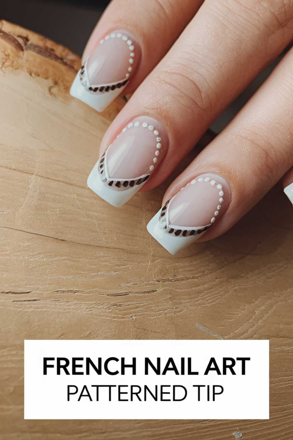Close-up of a hand with French manicure featuring patterned tips. The nails have white tips with dot and transparent zigzag designs. Background is a light wood texture. Text at the bottom reads, French Nail Art Patterned Tip.