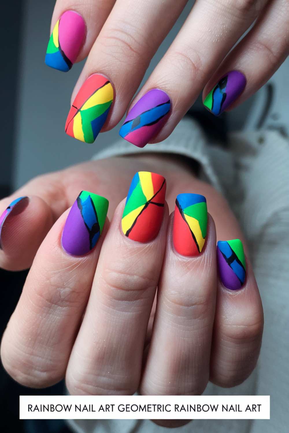 Close-up of hands showcasing stunning rainbow nail art. Each nail dazzles with vibrant geometric sections, divided by bold black lines to create a stained glass-like effect. The background is slightly blurred to make the intricate designs pop.