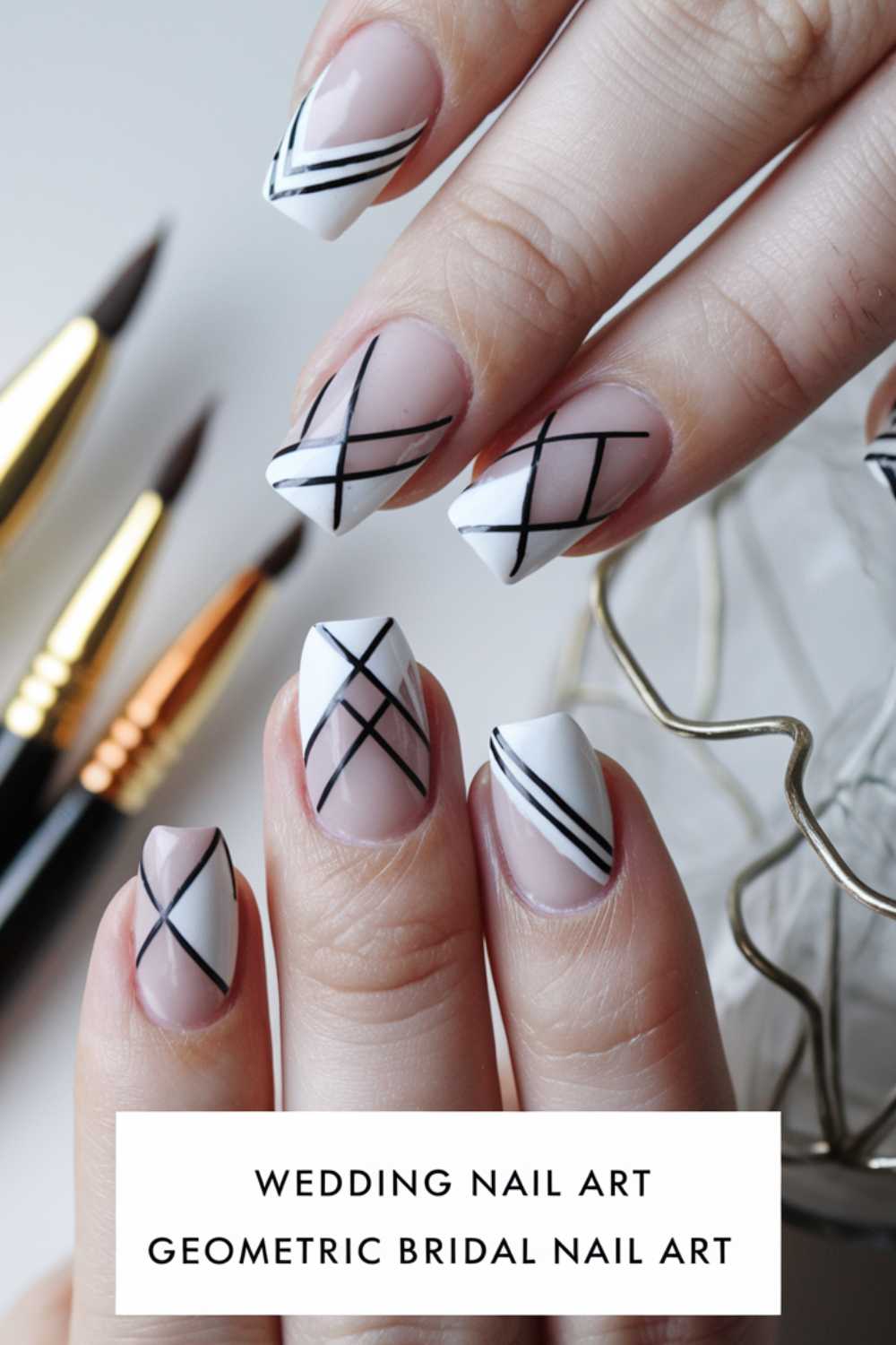 Close-up of hands with wedding-themed geometric nail art. Nails are white with pink accents, featuring black crisscross and diagonal lines. Three nail art brushes are in the background, and a decorative wire object is partially visible.