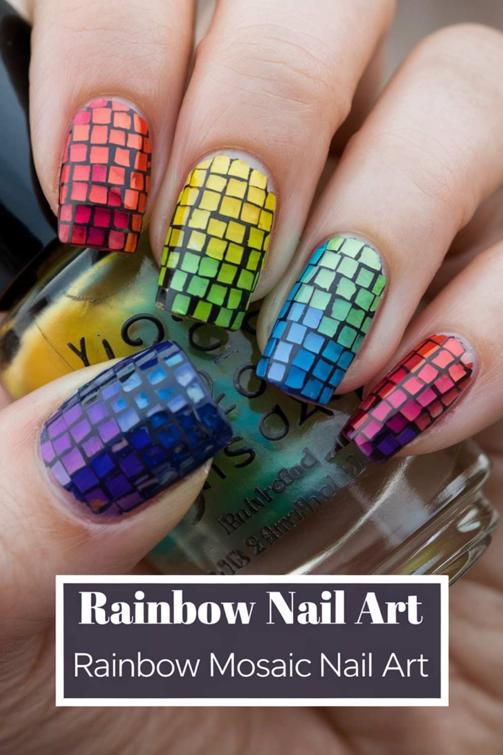 A close-up showcases a hand with stunning rainbow mosaic nail art. The design transitions from vibrant red at the cuticle to deep purple at the tip, embodying true Rainbow Nail Art magic. The hand elegantly holds a nail polish bottle, accentuating its colorful masterpiece.
