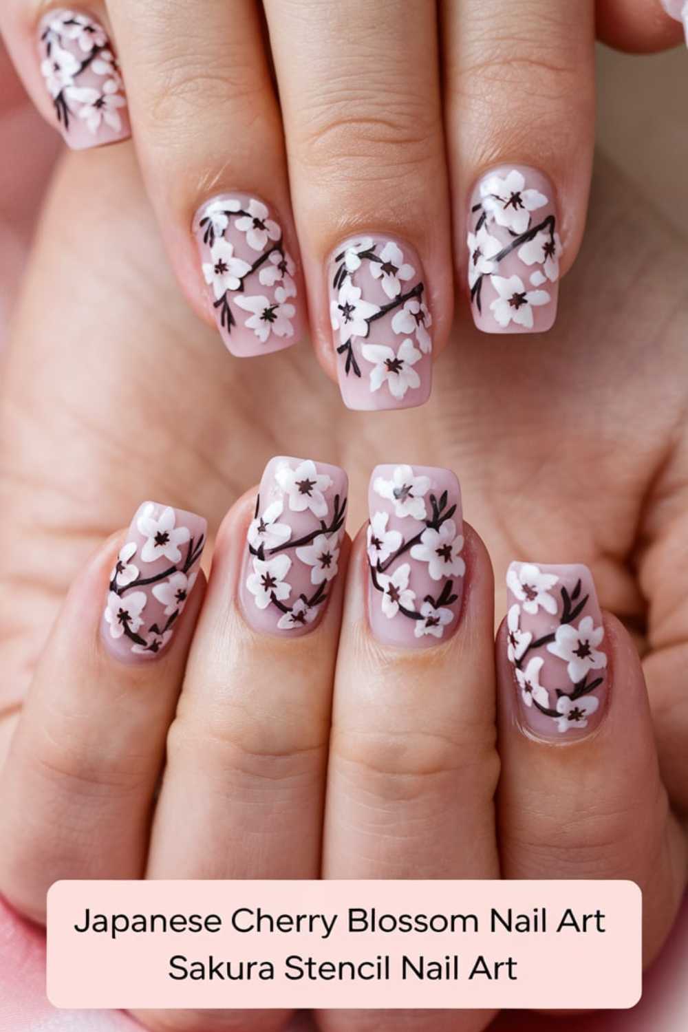 Close-up of hands with nails painted in light pink, adorned with intricate Japanese cherry blossom designs in white and brown. The image includes text: Japanese Cherry Blossom Nail Art, Sakura Stencil Nail Art.