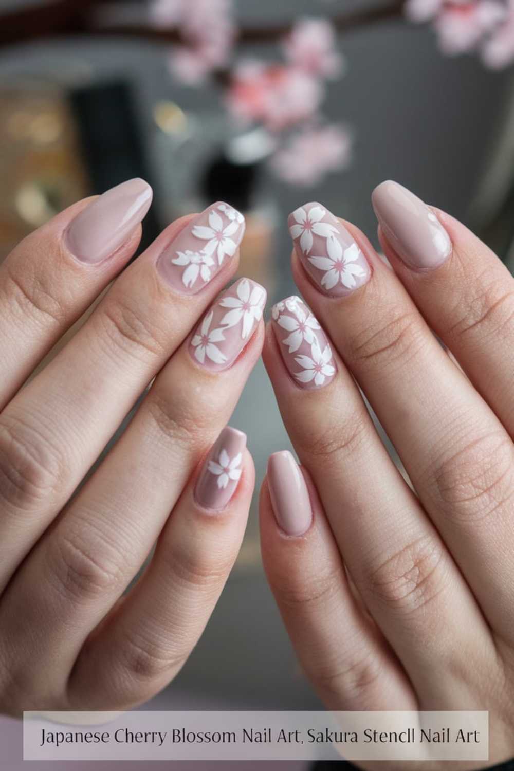 Close-up of hands showing nude-colored nails adorned with white cherry blossom designs. Nails are meticulously shaped and polished, with delicate floral patterns that accent a clean, elegant appearance.