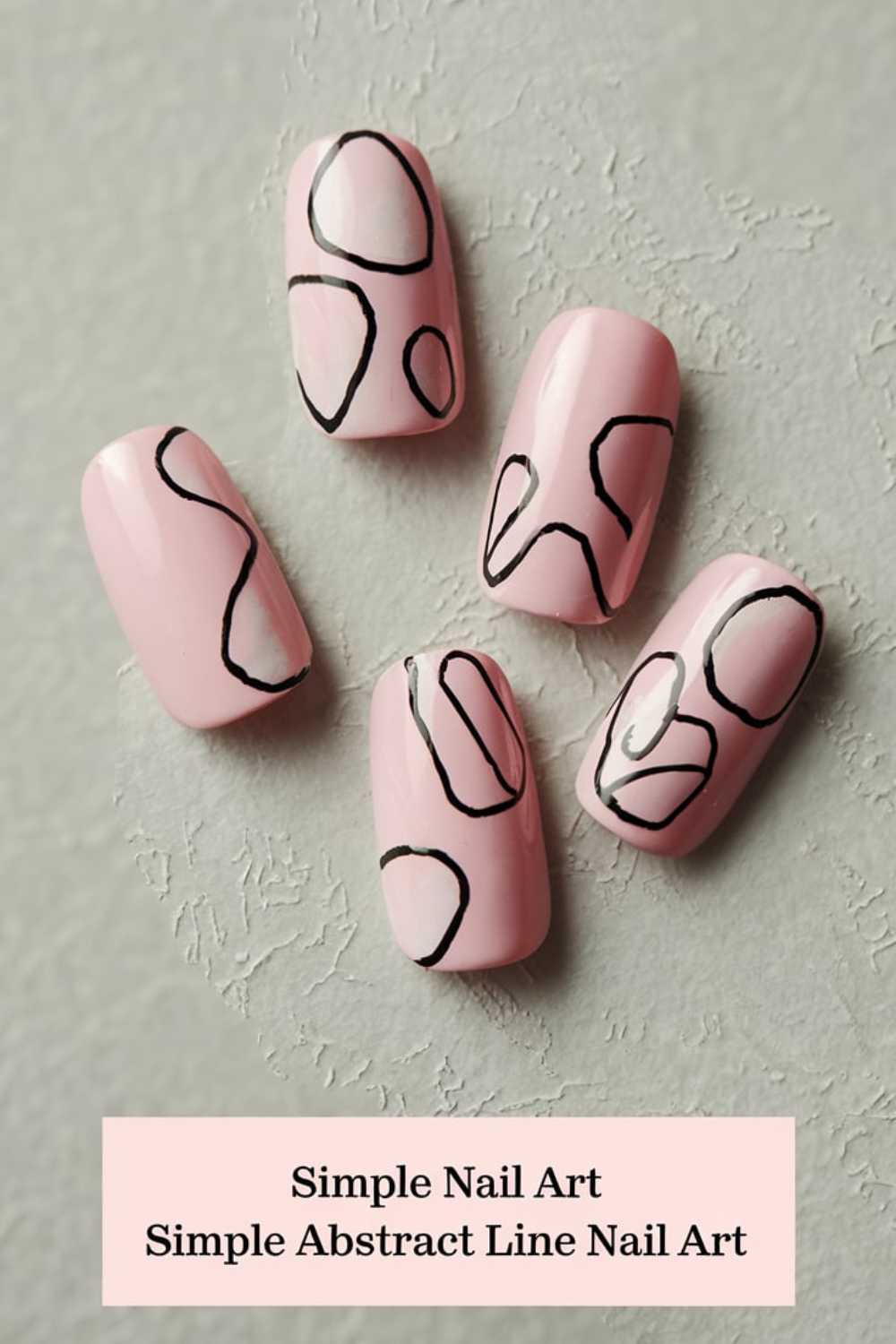 Pink nails adorned with simple black abstract line art are elegantly showcased against a textured gray background. A caption reads: Simple Nail Art, showcasing the beauty of minimalist style.