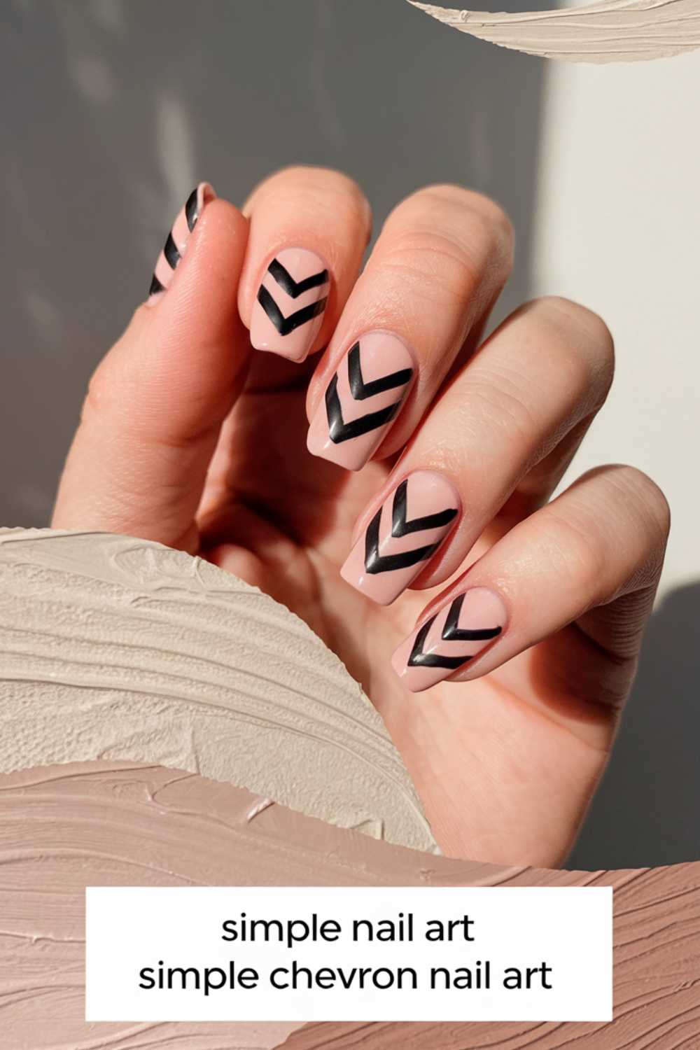 A hand with a glossy nude manicure features simple black chevron stripes. The fingers are elegantly poised against a textured, neutral background. Text at the bottom reads: simple nail art, simple chevron nail art.