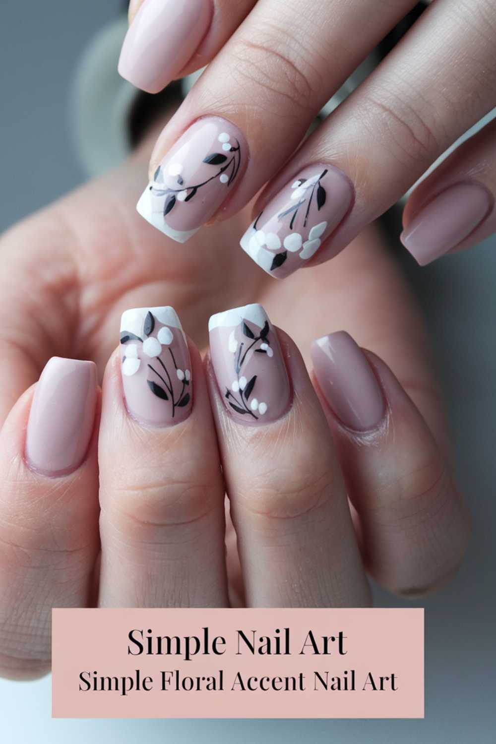 A close-up of a hand displays simple nail art: pink nails with white tips, adorned with delicate black branches and white flowers. At the bottom, Simple Nail Art: Simple Floral Accent Nail Art elegantly underscores the designs charm.