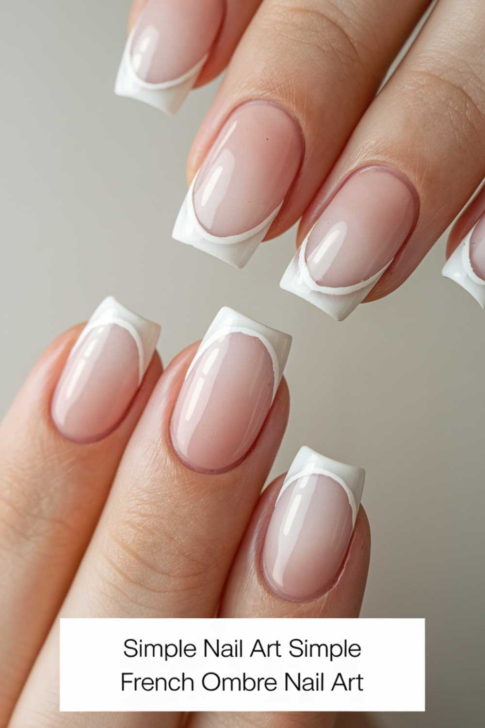 Close-up of fingers with simple French ombre nail art. The nails display a subtle gradient from natural pink to white tips, creating a chic and elegant appearance.