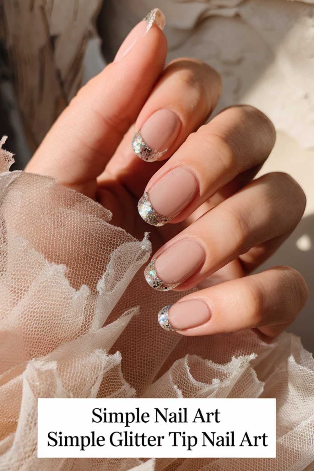 Close-up of a hand with nude-colored nails featuring glittery tips, showcasing a chic and effortless design. The hand rests on a soft, textured fabric. Text at the bottom reads Simple Glitter Tip Nail Art - perfect for those who appreciate simple nail art elegance.