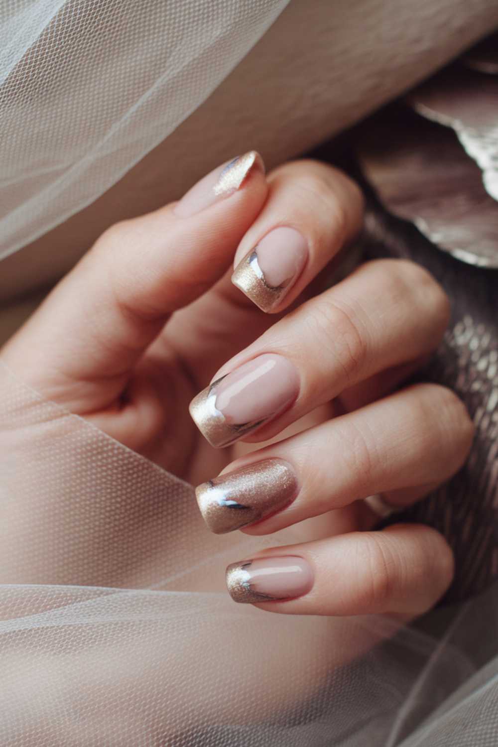 Close-up of a hand showcasing simple nail art—nude almond-shaped nails with metallic gold tips. Partially wrapped in sheer fabric, the look exudes elegance and sophistication.