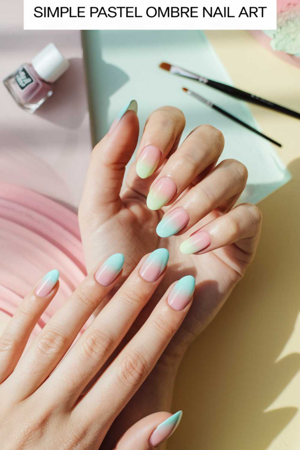 Hands showcasing simple pastel ombre nail art in shades of pink, yellow, and blue. A nail polish bottle and brush are visible in the background on a soft pastel-colored surface, perfectly capturing the essence of simple nail art.