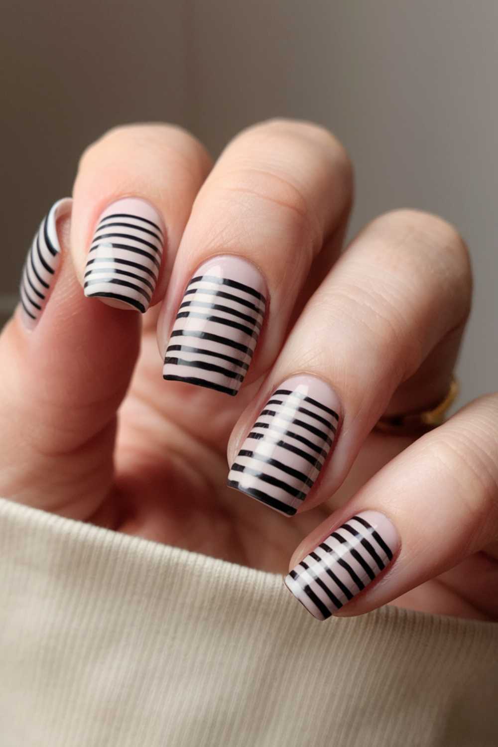 Featuring a simple nail art design, a hand with nails painted in a minimalist style showcases a clear base adorned with horizontal black stripes of varying thickness. The coffin-shaped nails complement the light skin tone beautifully.