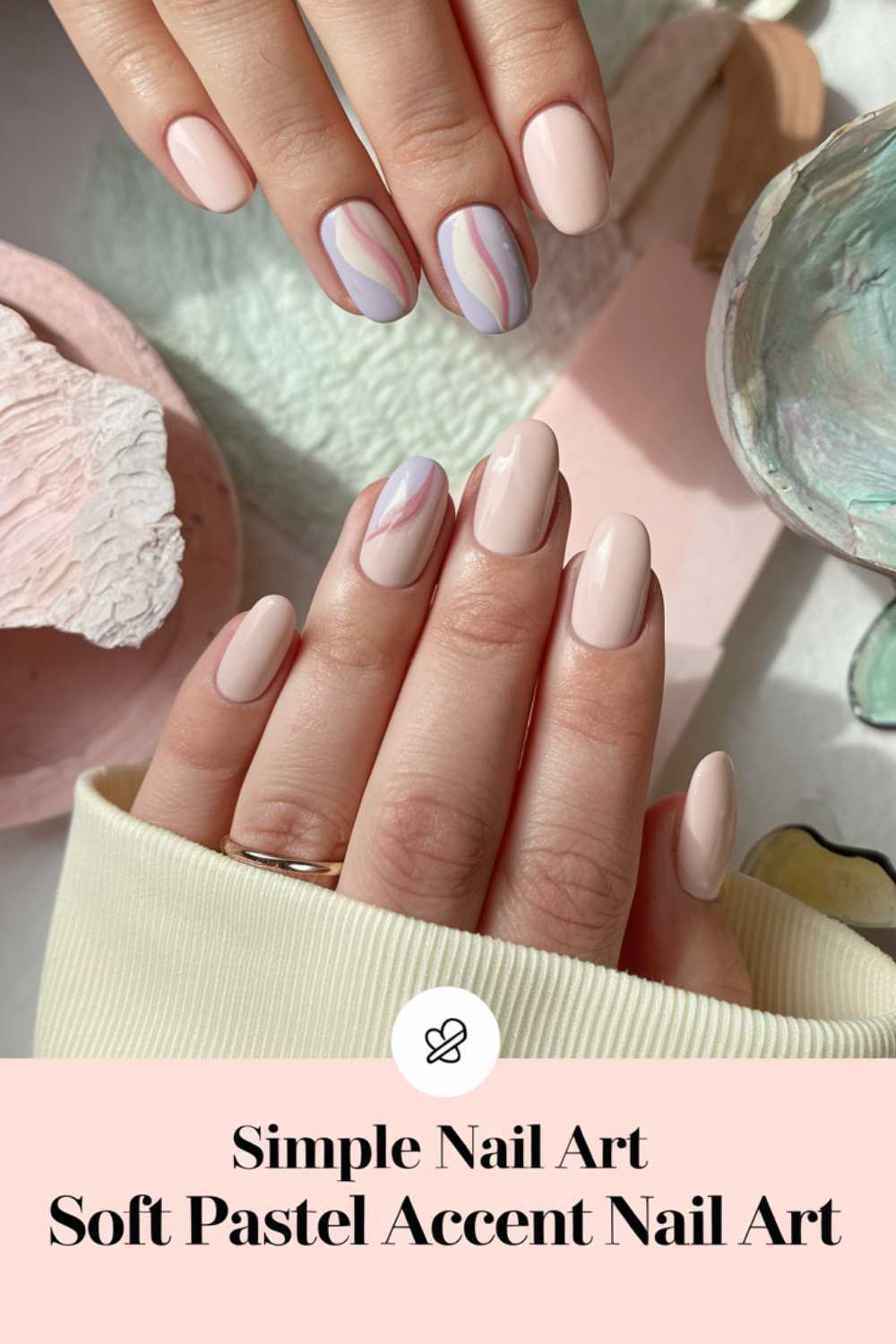 A close-up of hands with manicured nails showcases simple nail art with pastel pink and purple accents. One hand rests on a textured surface surrounded by pastel decorations. Below the image, the text reads Soft Pastel Accent Nail Art.