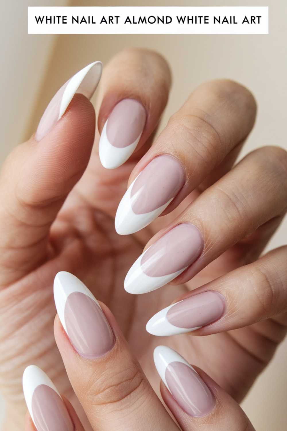 Close-up of a hand with almond-shaped nails featuring a French manicure. The nails are pale pink with crisp white tips. Fingers are elegantly positioned, showcasing the polished and stylish nail design against a neutral background.