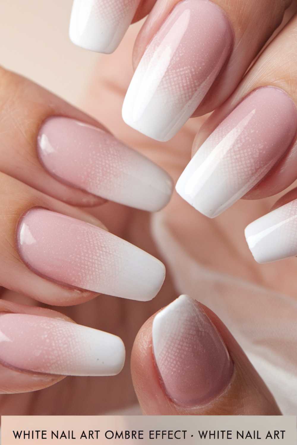 Close-up of hands showing nails with an ombre effect manicure. The gradient transitions from soft pink at the cuticle to white at the tips, creating a smooth and elegant appearance.