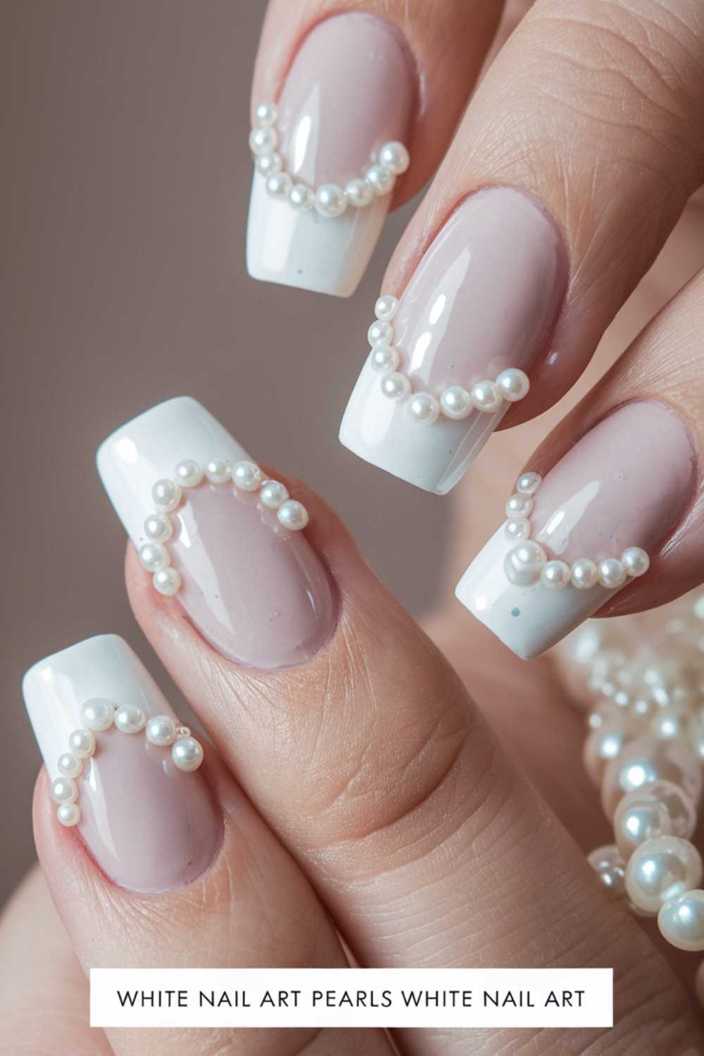 Close-up of a hand with elegant white French manicure adorned with small white pearls. The pearls form delicate patterns on each nail, adding a sophisticated touch.