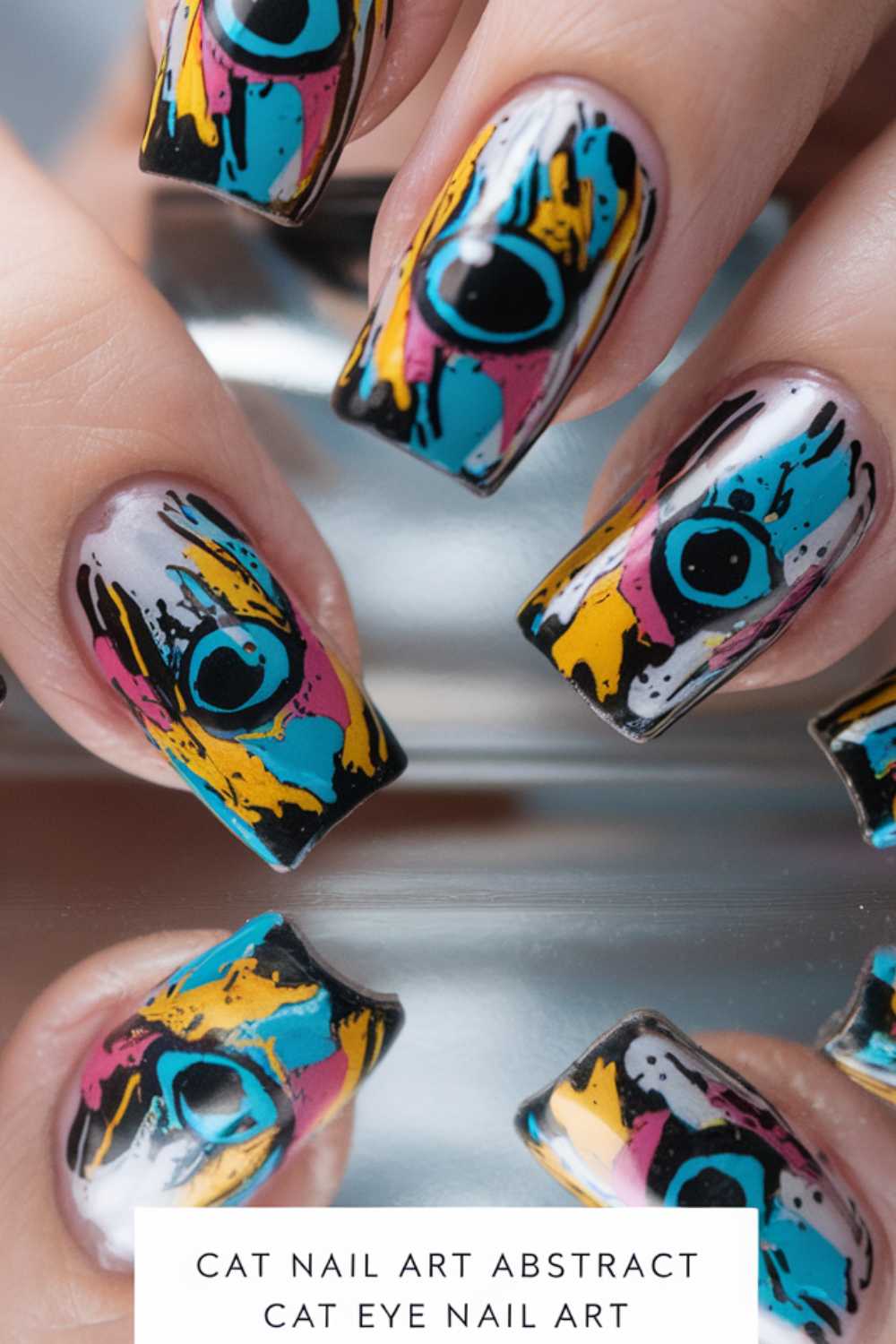 Close-up of fingers showcasing a vibrant, abstract cat eye nail art design. The nails feature a mix of blue, pink, yellow, and black on a metallic silver base, creating a striking and artistic appearance. Reflected on a shiny surface below.