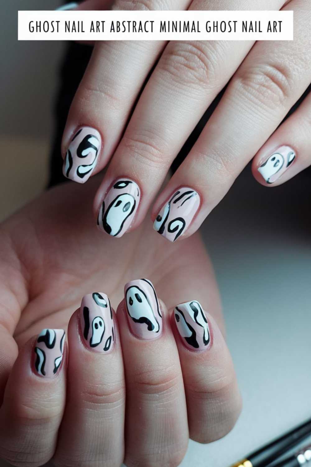 Close-up of hands showing Halloween-themed nail art with abstract black and white ghost designs on a nude base. The nails have a minimalist and artistic style, with each nail uniquely featuring ghostly shapes.