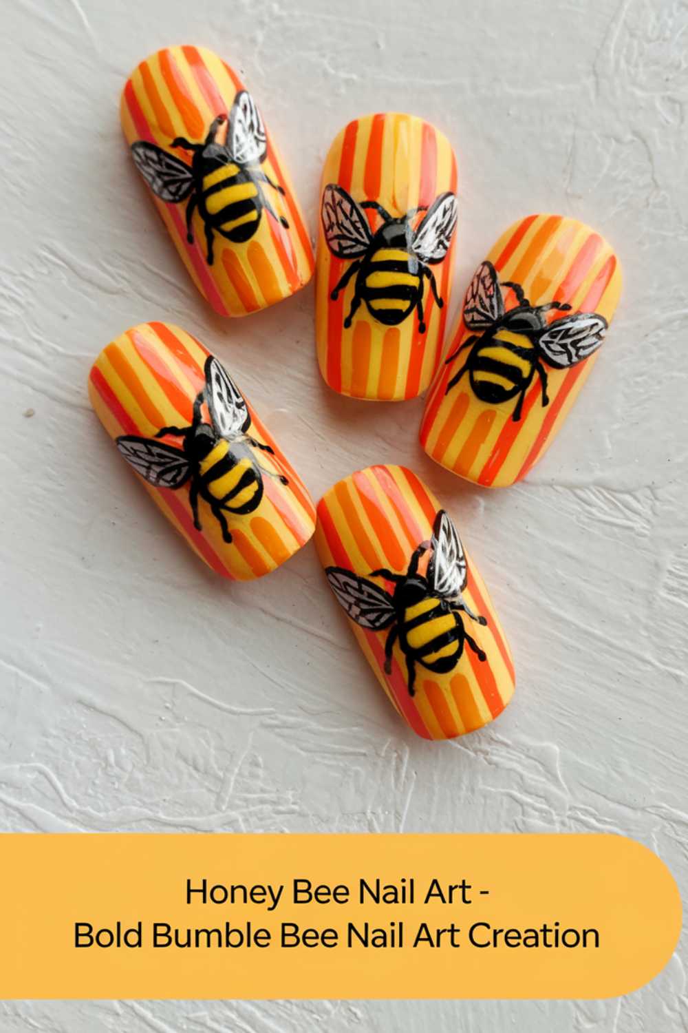 Five artificial nails with yellow and orange vertical stripes showcase intricate black and yellow bee designs. They are arranged on a textured white surface. A text box reads: Bold Bee Nail Art - Bumble Bee Nail Art Creation.