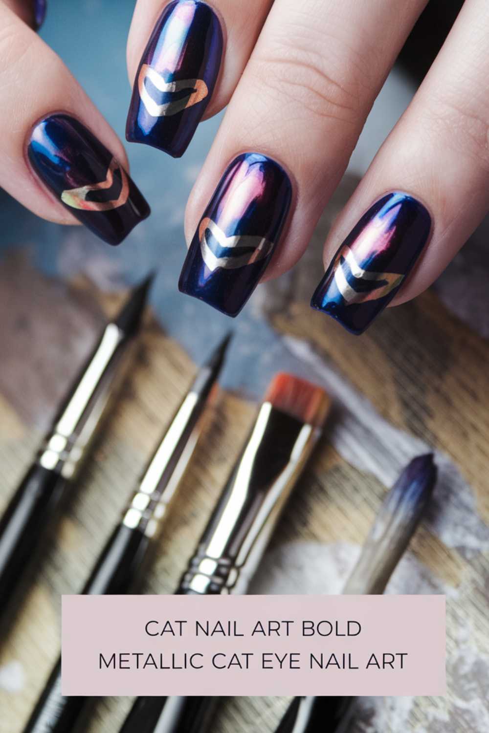 Close-up of hands with metallic cat eye nail art in dark blue and pink hues. The nails have a chevron pattern. Below the hands, there are several nail art brushes. A label reads, Cat Nail Art Bold Metallic Cat Eye Nail Art.