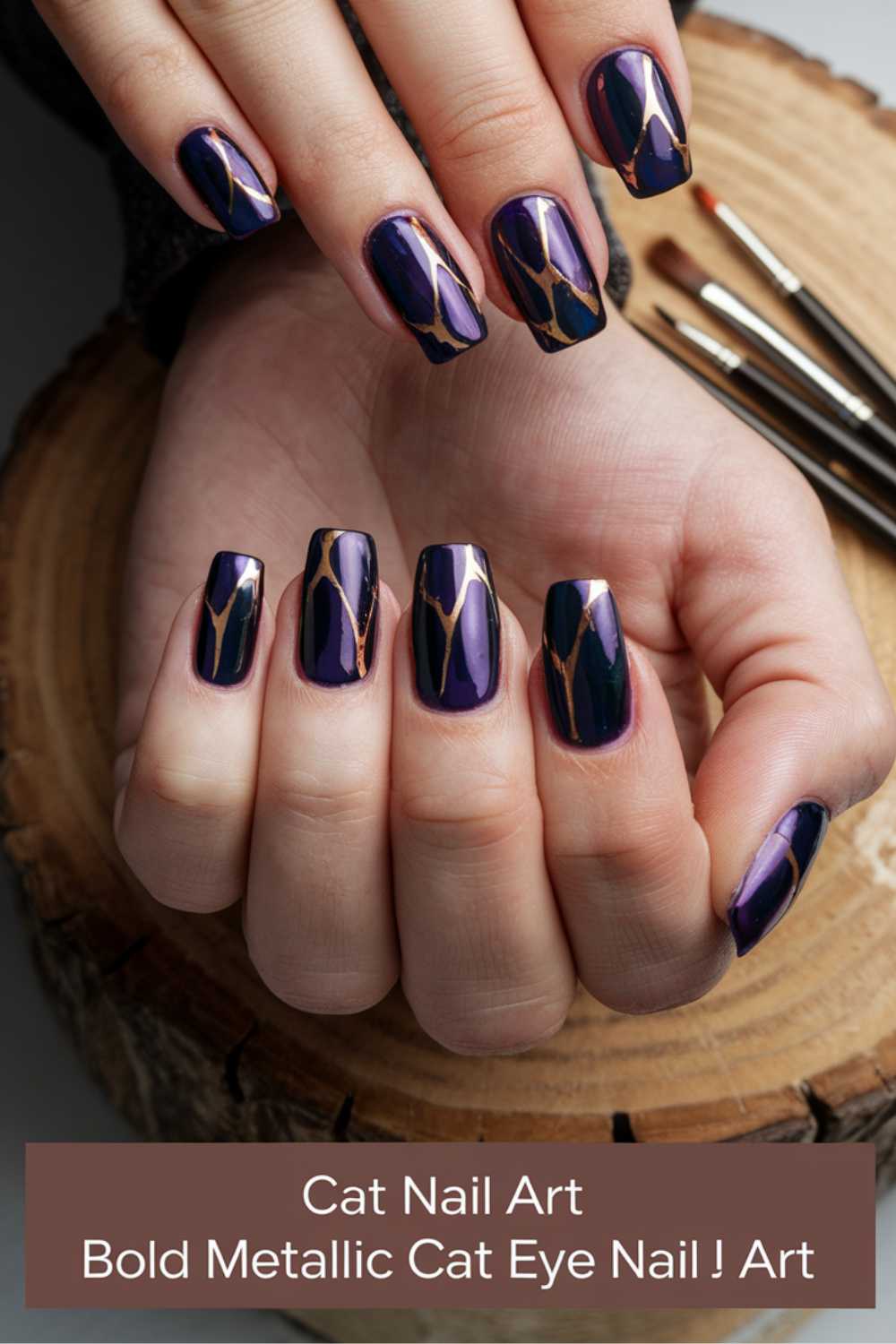 Close-up of hands with bold metallic cat eye nail art. Nails have a dark purple hue with shiny, reflective edges and gold geometric accents. Nail art brushes are in the background. Text at the bottom reads: Cat Nail Art Bold Metallic Cat Eye Nail J Art.