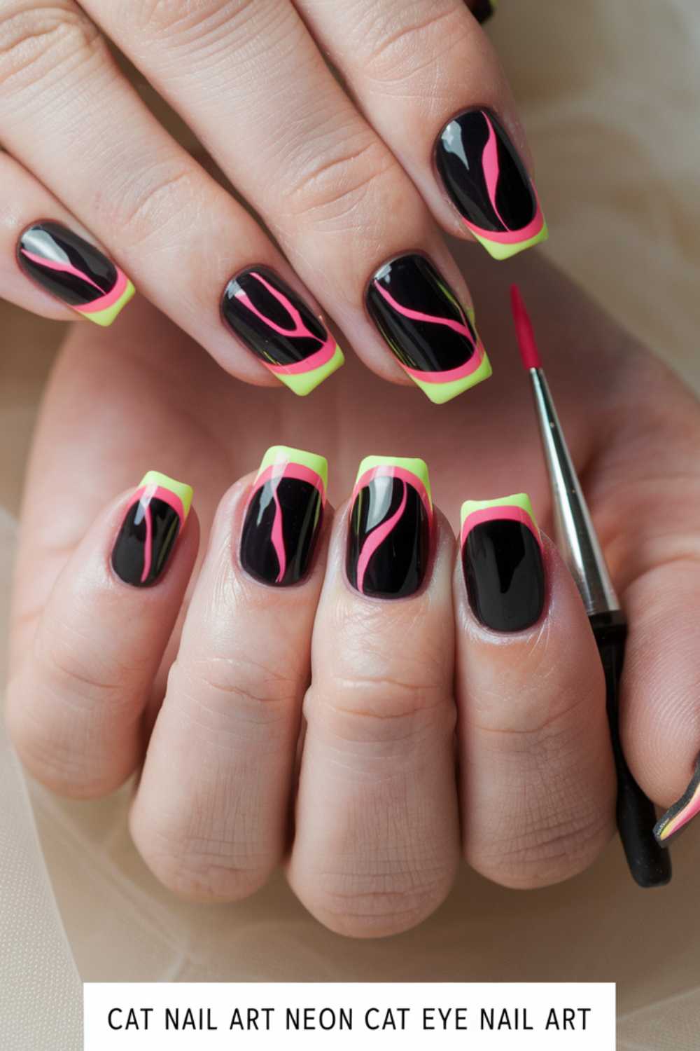 A close-up of hands with black manicured nails featuring neon green French tips and pink wavy lines. The hands hold a small nail art brush.