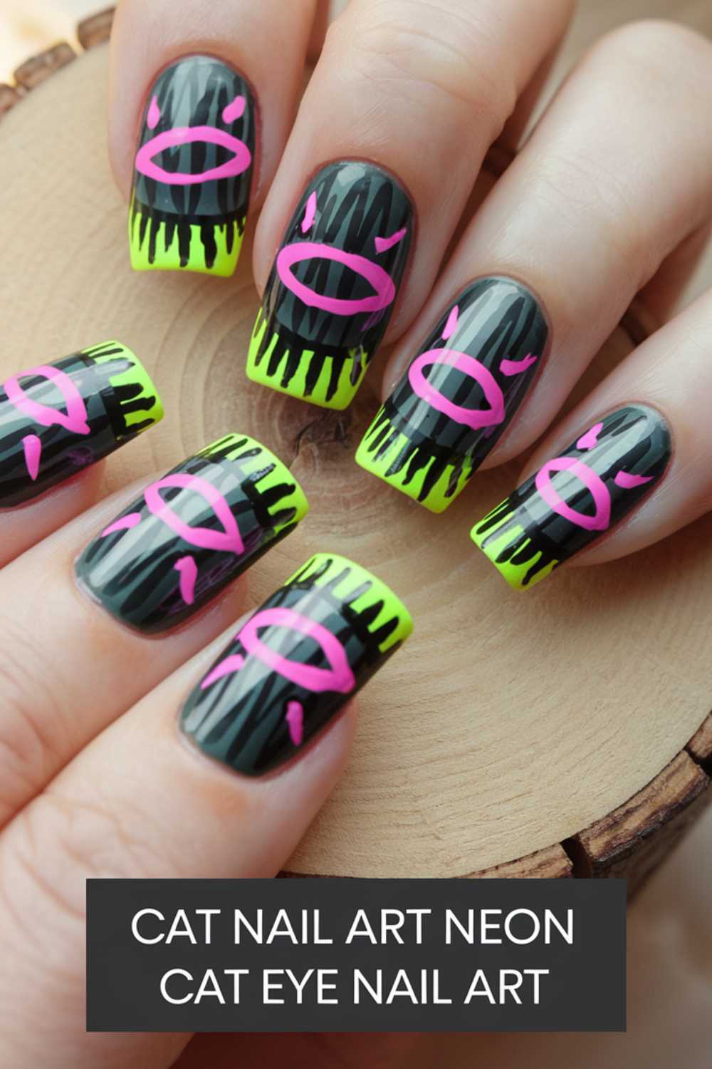 Close-up of hands with cat-themed neon nail art. Nails feature black and neon green backgrounds with pink cat eye designs. Nails are displayed on a wooden surface.