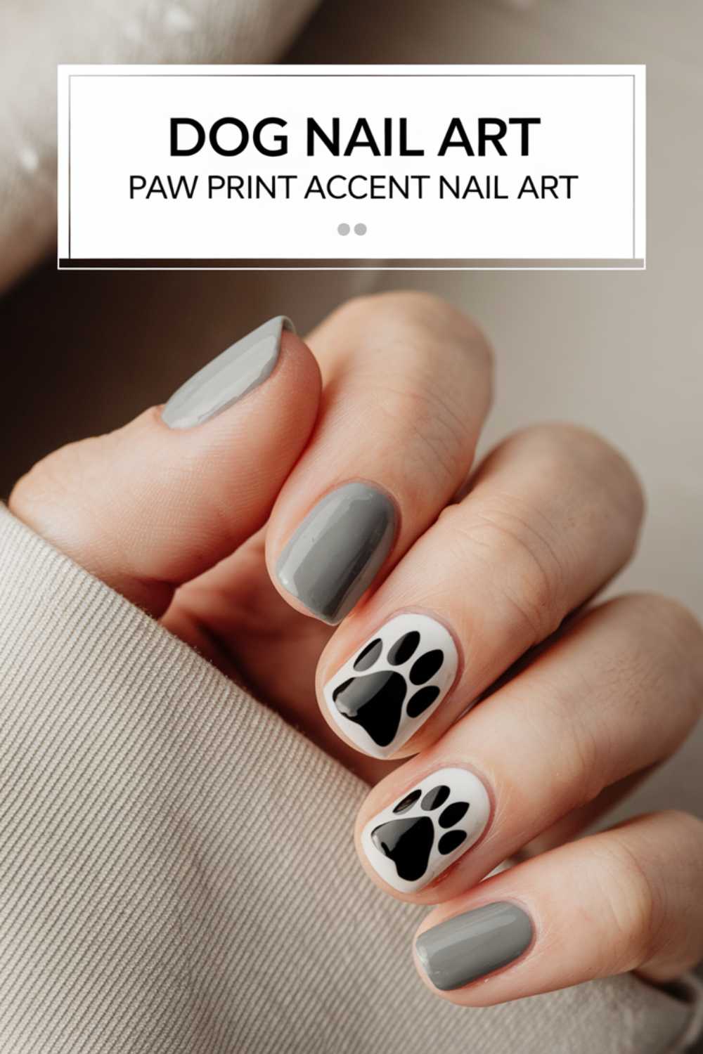 A hand showcases elegant gray nail polish, adorned with black paw print designs on the middle and ring fingernails. This stylish Dog Nail Art makes a paw-sitive statement with its charming Paw Print Accent Nail design.