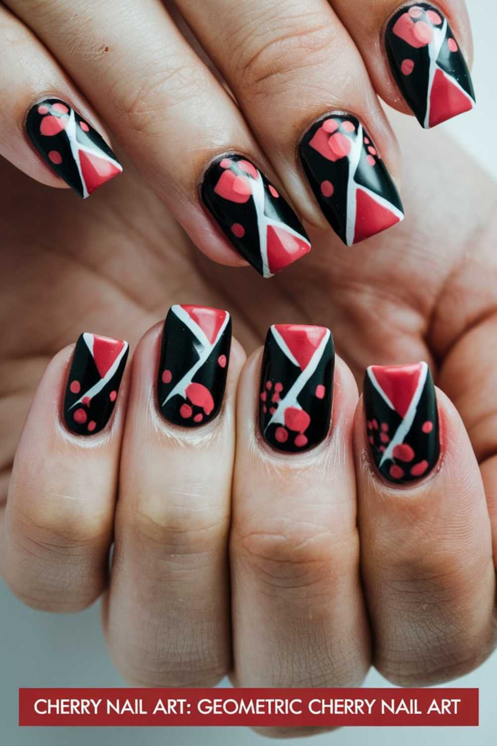 Fingernails painted with a black base showcasing red cherries, white diagonal lines, and geometric patterns. Small circular red accents add detail. Below, text reads: Cherry Nail Art Designs - Geometric Cherry Nail Art.