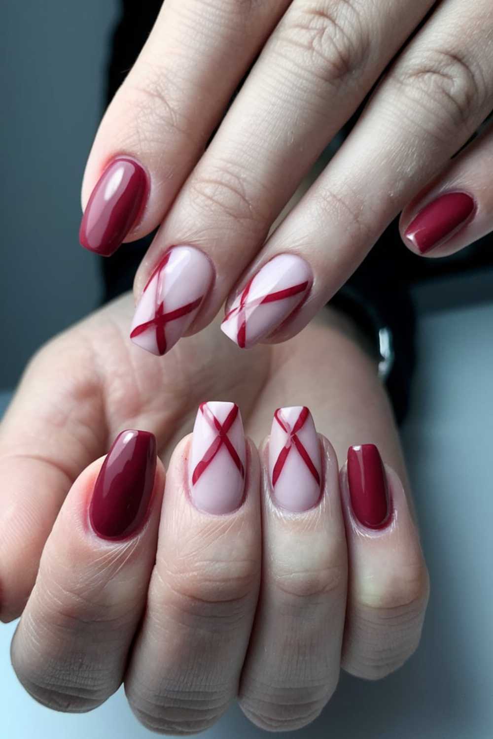 Close-up of a hand showcasing a beautiful cherry nail art design with alternating maroon nails and light pink nails adorned with maroon crisscross lines. The neatly shaped nails stand out against a neutral background, exuding elegance.