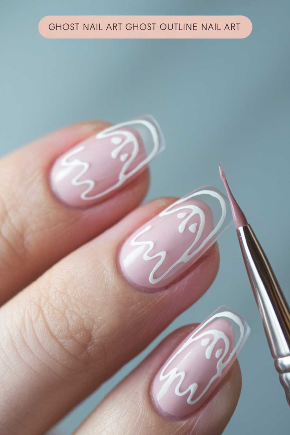 Close-up of fingers with pink nails featuring white ghost outline nail art. A small brush is applying final touches to the design. Text above reads, Ghost nail art ghost outline nail art.