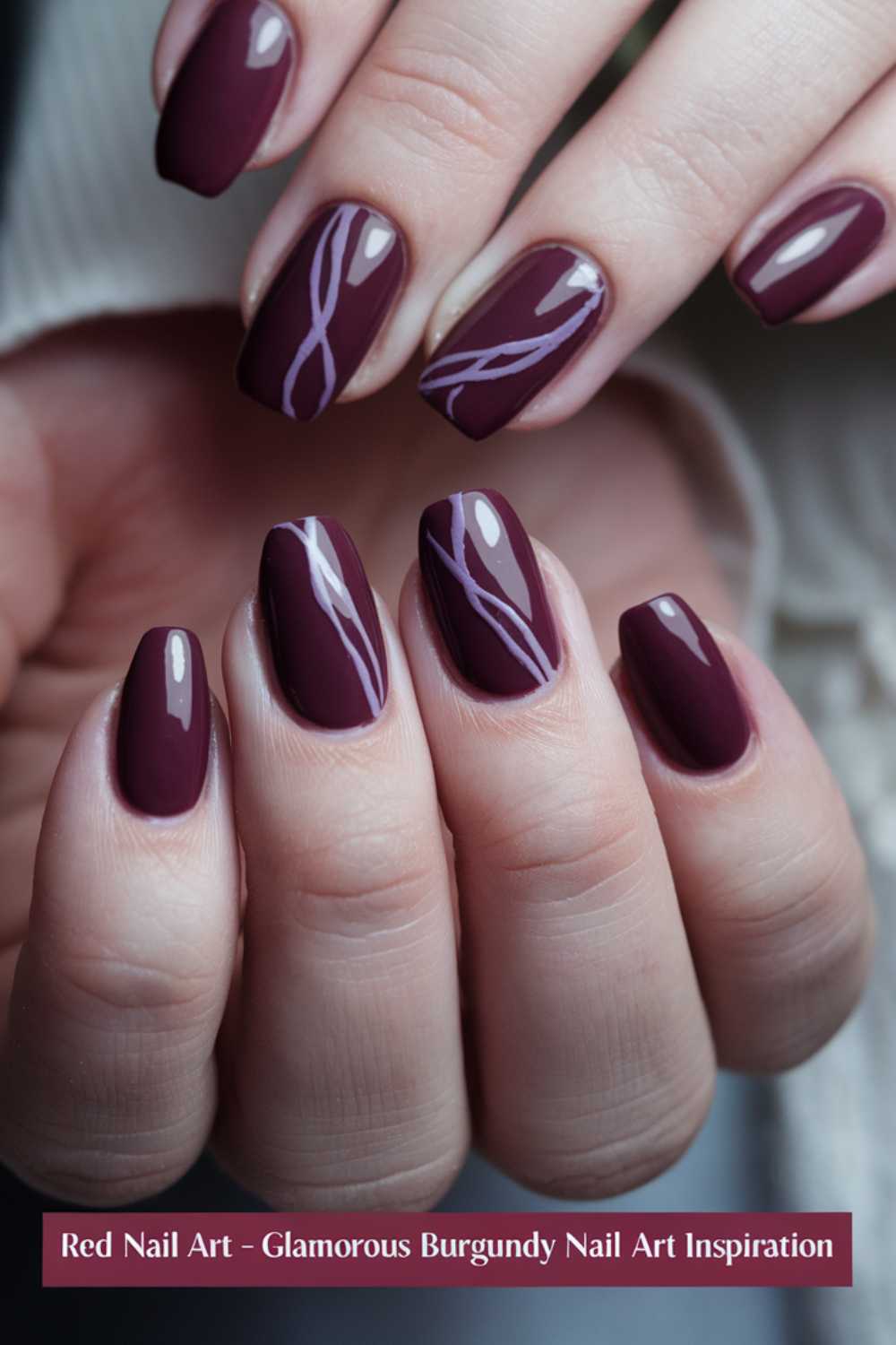 Close-up of hands with glossy burgundy nail polish. Nails feature a stylish swirl design in a lighter shade. Text at the bottom reads: Red Nail Art - Glamorous Burgundy Nail Art Inspiration.