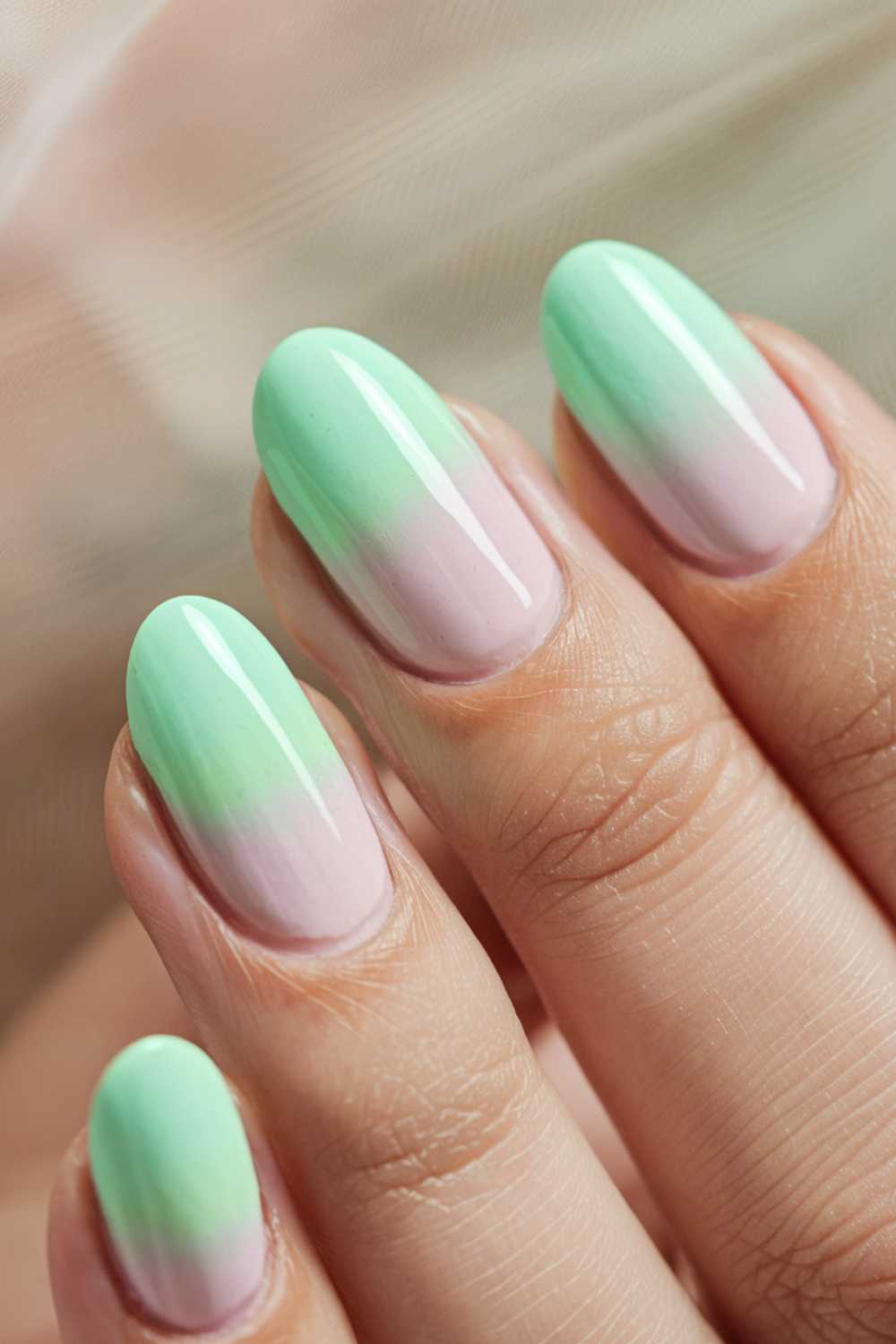A close-up of a hand with almond-shaped nails featuring green nail art in a beautiful green and light pink ombre manicure.