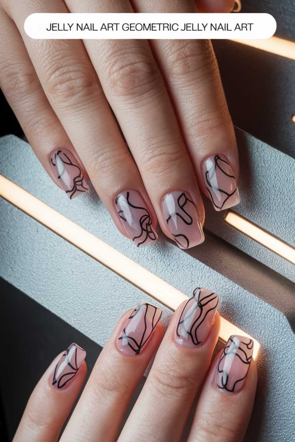 Close-up of hands showcasing jelly nail art ideas. The nails feature a translucent pink base with abstract black line designs. This creative artistry is set against a textured, illuminated surface, adding an extra layer of brilliance to the scene.