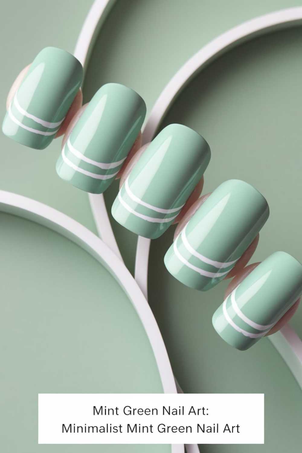 Mint green artificial nails with a glossy finish are arranged in a row, showcasing elegant green nail art. Each nail features two thin, white horizontal lines near the tips, set against a coordinating mint green background with white curved lines.