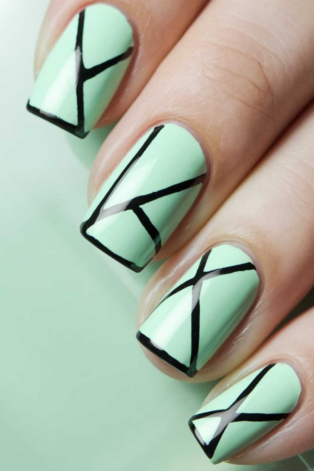 Close-up of fingernails painted mint green, featuring Green Nail Art with black geometric lines forming angular shapes and patterns on each nail.