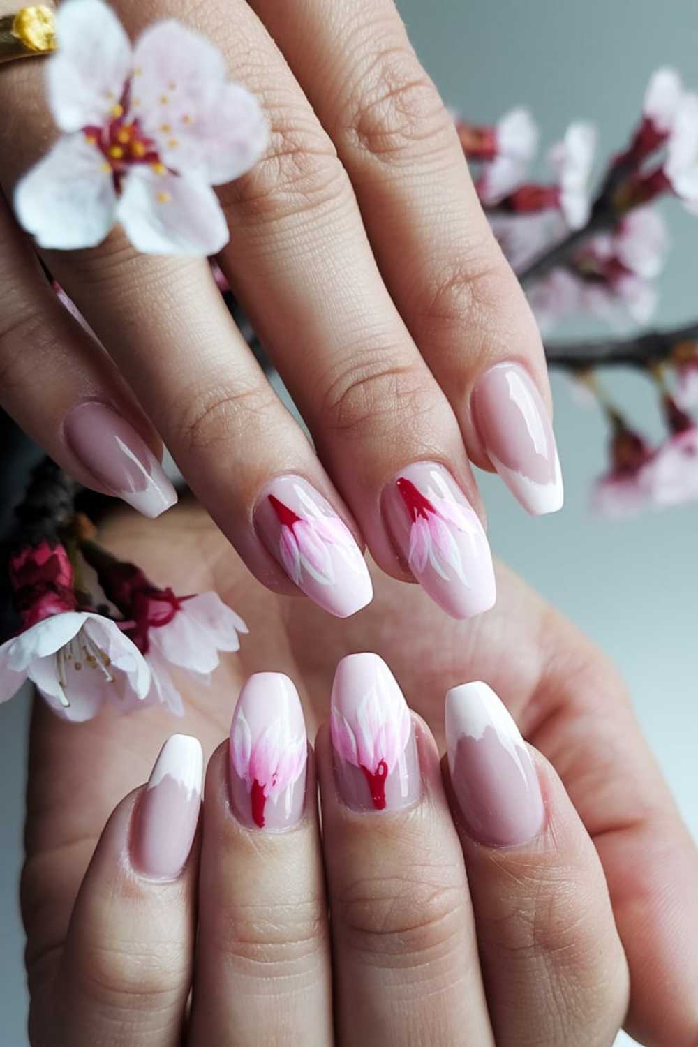 Close-up of hands showcasing a manicure with cherry nail art designs. The almond-shaped nails feature a gradient of light pink and white, adorned with delicate cherry blossom patterns. A branch of blossoms in the background perfectly complements the elegant theme.